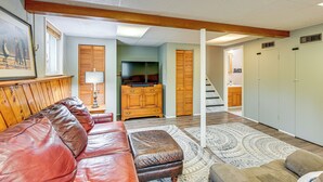 A spacious living room with a leather sofa, ottoman, and a patterned rug. A wooden cabinet and a television are visible in the background. - 1 Mi to Dtwn: Suburban Home w/ Yard in Owosso (Owosso)