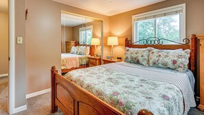 A bedroom with a wooden bed, a large mirror, a window with blinds, and a ceiling fan. - 1 Mi to Dtwn: Suburban Home w/ Yard in Owosso (Owosso)