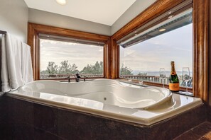 Une grande baignoire sur pieds, placée dans une pièce aux boiseries apparentes, offrant une vue sur les arbres et les montagnes grâce à de grandes fenêtres.