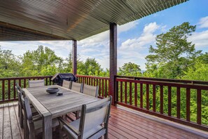 Une terrasse en bois avec une table et des chaises, un barbecue et une vue sur les arbres.