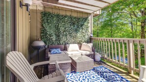 A covered outdoor seating area with wicker furniture, a patterned rug, and a wall of greenery.