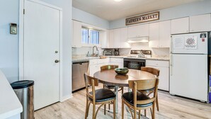 A kitchen with white cabinets, a wooden dining table, and chairs. There is a sign above the cabinets that reads "FARMER'S MARKET".