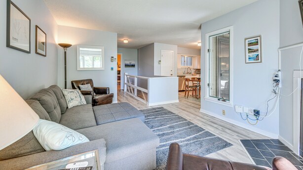 A modern living room with a sofa, armchairs, and a coffee table. There is a kitchen area with cabinets and a dining table.