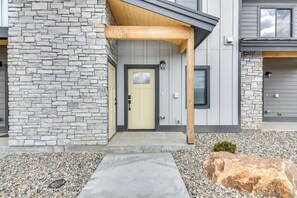 A modern two-story house with a stone facade, a wooden porch, and a concrete pathway leading to the entrance.