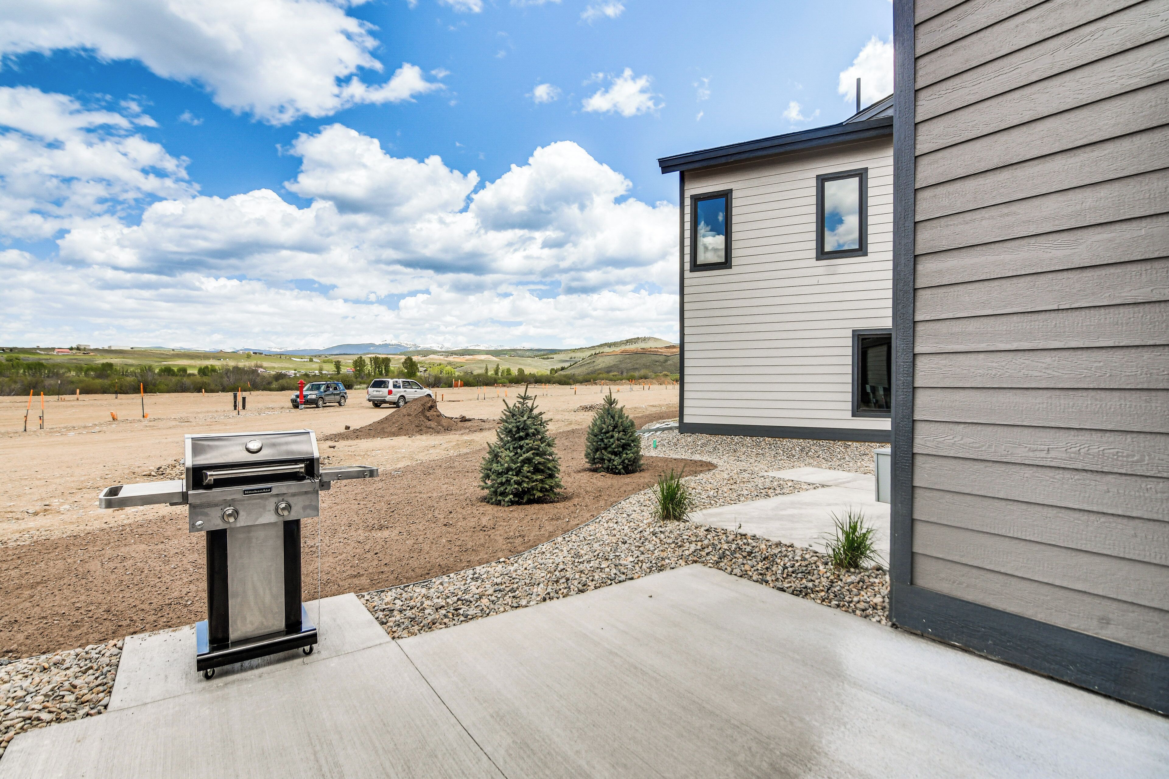 Ein modernes Haus mit Terrasse, Grill, kleinen Bäumen und blauem Himmel.