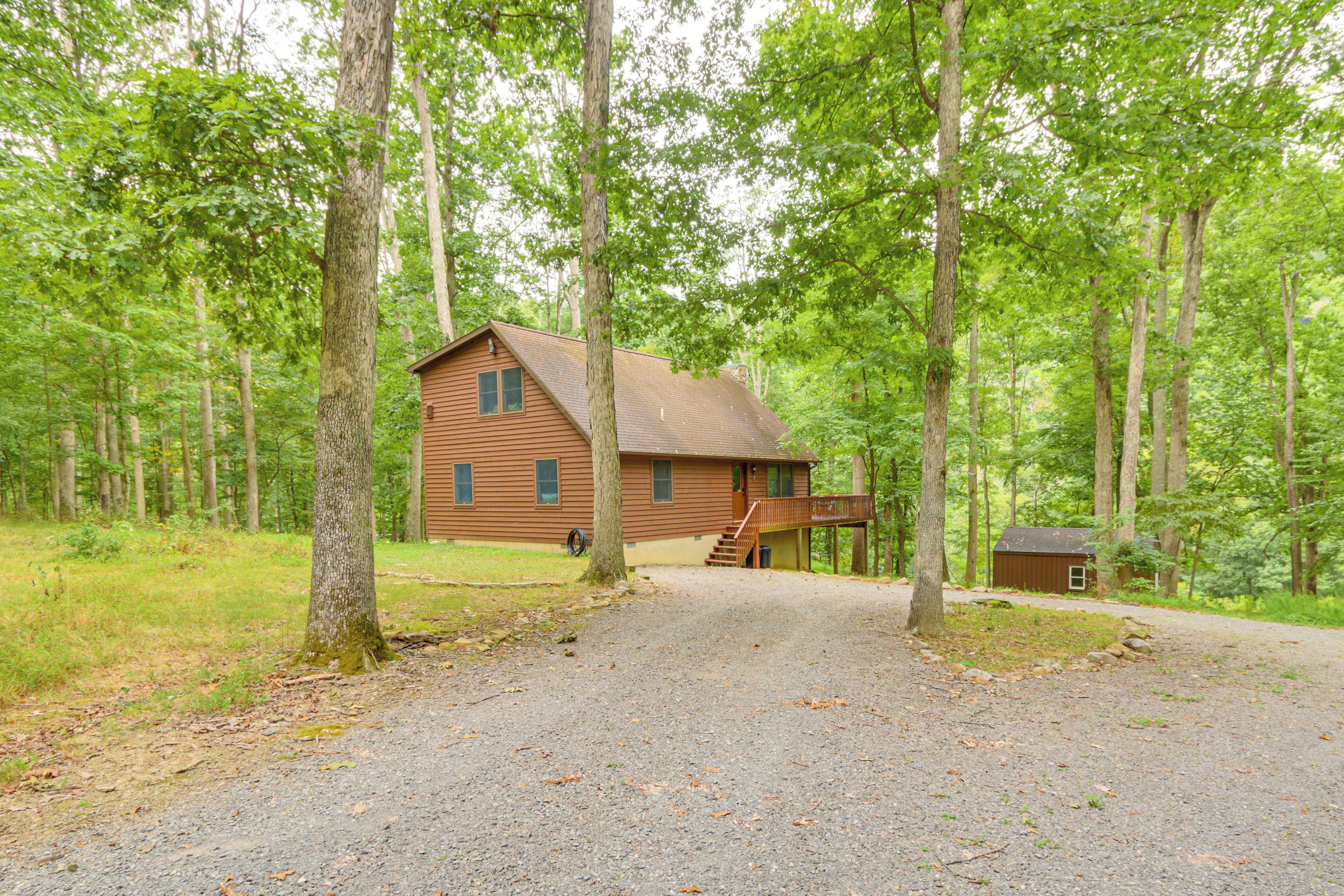 A wooden cabin with a porch and a small shed in a forested area.