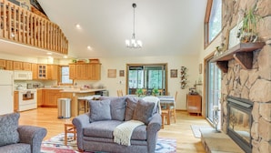 A spacious living area with a fireplace, a dining area, and a kitchen with wooden cabinets. - Great Cacapon Mtn Cabin w/ Private Hot Tub + Views (Great Cacapon)