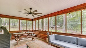 A wooden cabin with a large window, a ceiling fan, a wooden bench, a sofa, and a picnic table. - Great Cacapon Mtn Cabin w/ Private Hot Tub + Views (Great Cacapon)