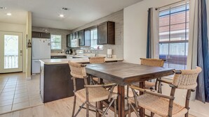A modern kitchen with dark cabinets, a central island, and a dining area with woven chairs.