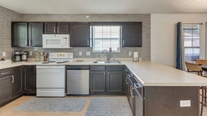 A modern kitchen with dark cabinets, a white microwave, stainless steel appliances, and a large window.