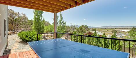 An outdoor ping pong table under a wooden pergola with a view of a rural landscape.