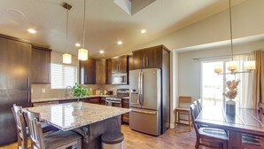 A modern kitchen with dark wood cabinets, stainless steel appliances, a granite countertop island, and a dining area with a wooden table and chairs. - Panoramic Views: Spacious Home in Cedar City! (Cedar City)