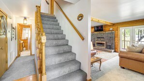 A staircase with a wooden handrail leading to a living room with a stone fireplace, a brown leather sofa, and a television mounted above the fireplace. - Lakeside Cabin w/ Lake & Boat Ramp Access Nearby (Spavinaw)