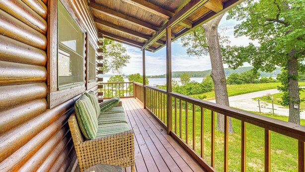 A wooden deck with a bench and a wicker chair, overlooking a grassy area with trees and a distant view. - Lakeside Cabin w/ Lake & Boat Ramp Access Nearby (Spavinaw)