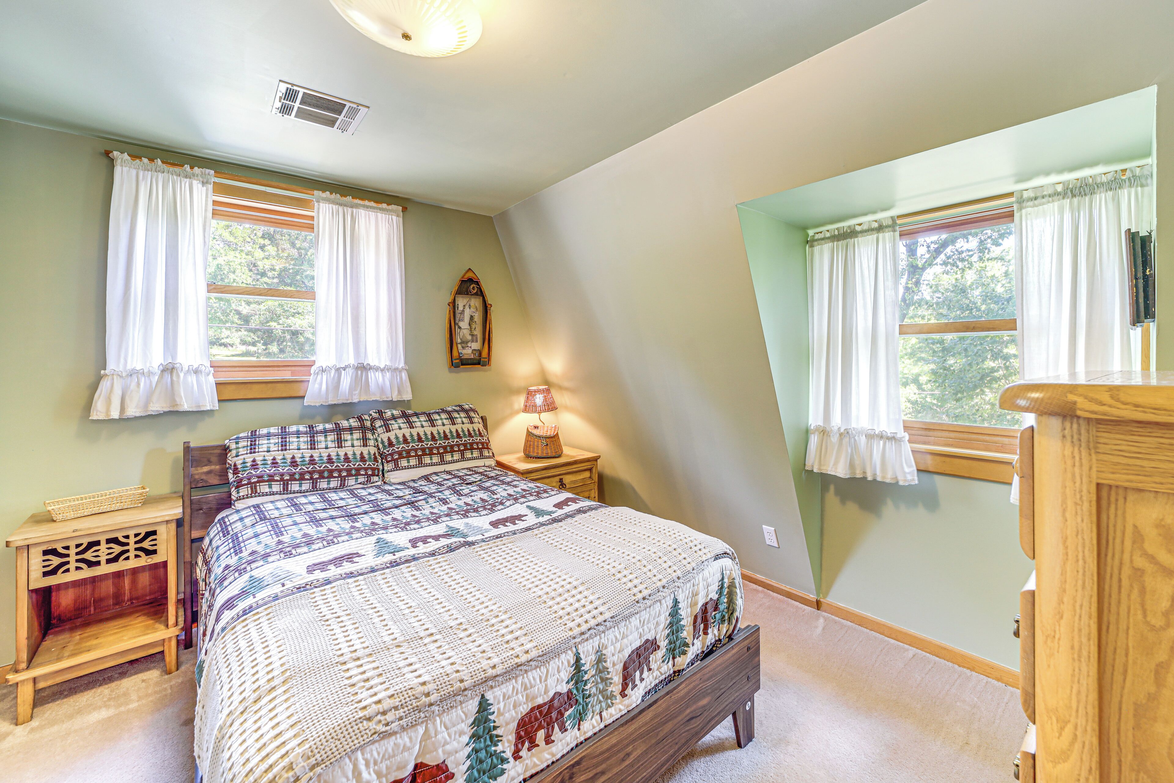 A bedroom with a large bed, two nightstands, a wooden dresser, and a window with curtains.