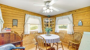 A wooden-paneled room with a round table, four chairs, a ceiling fan, and windows with curtains. - Lakeside Cabin w/ Lake & Boat Ramp Access Nearby (Spavinaw)