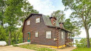 A log cabin with a porch, a green door, and a view of the water. - Lakeside Cabin w/ Lake & Boat Ramp Access Nearby (Spavinaw)