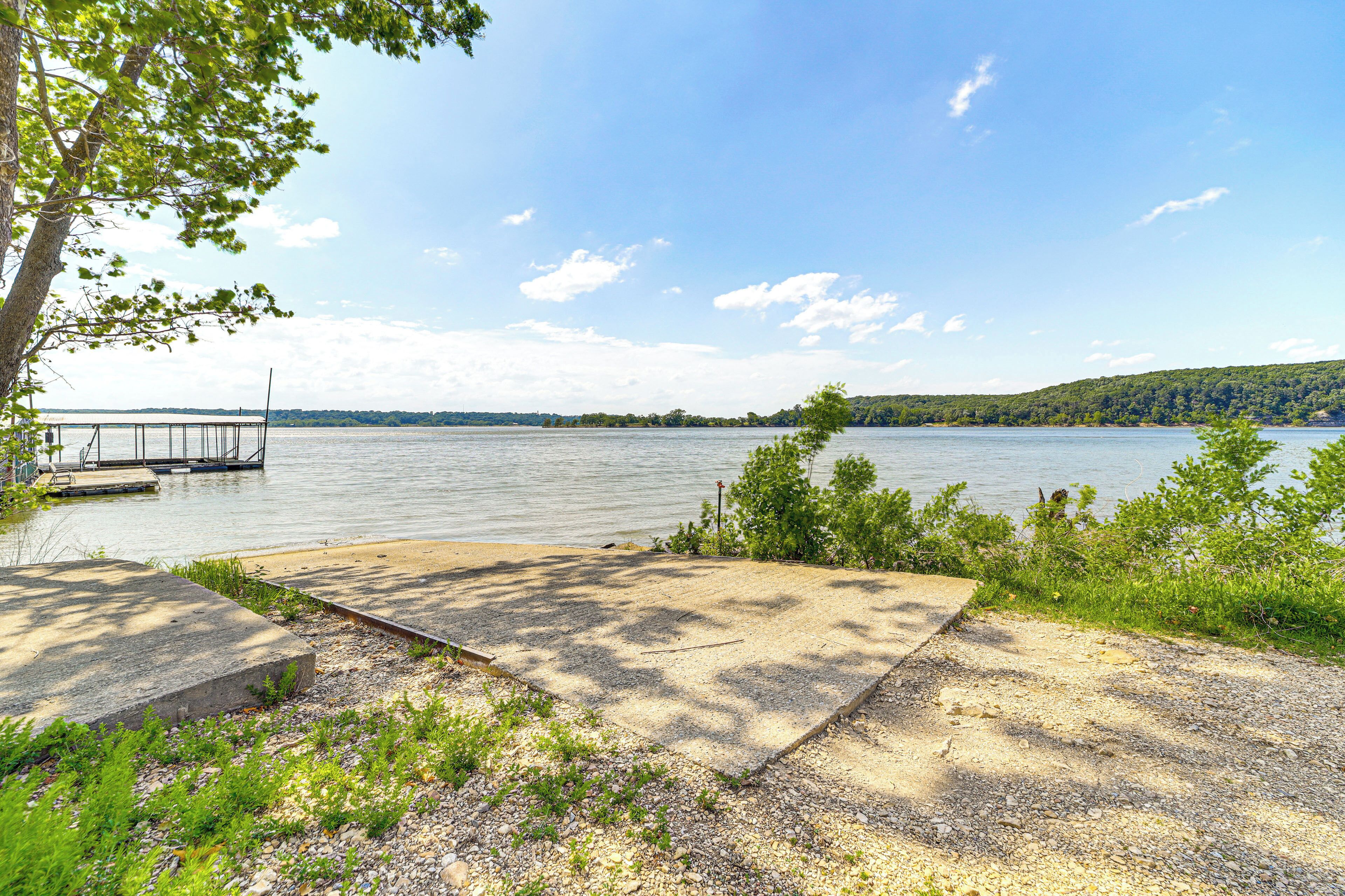 A lakeside deck with a concrete platform, surrounded by greenery and a dock extending into the water.