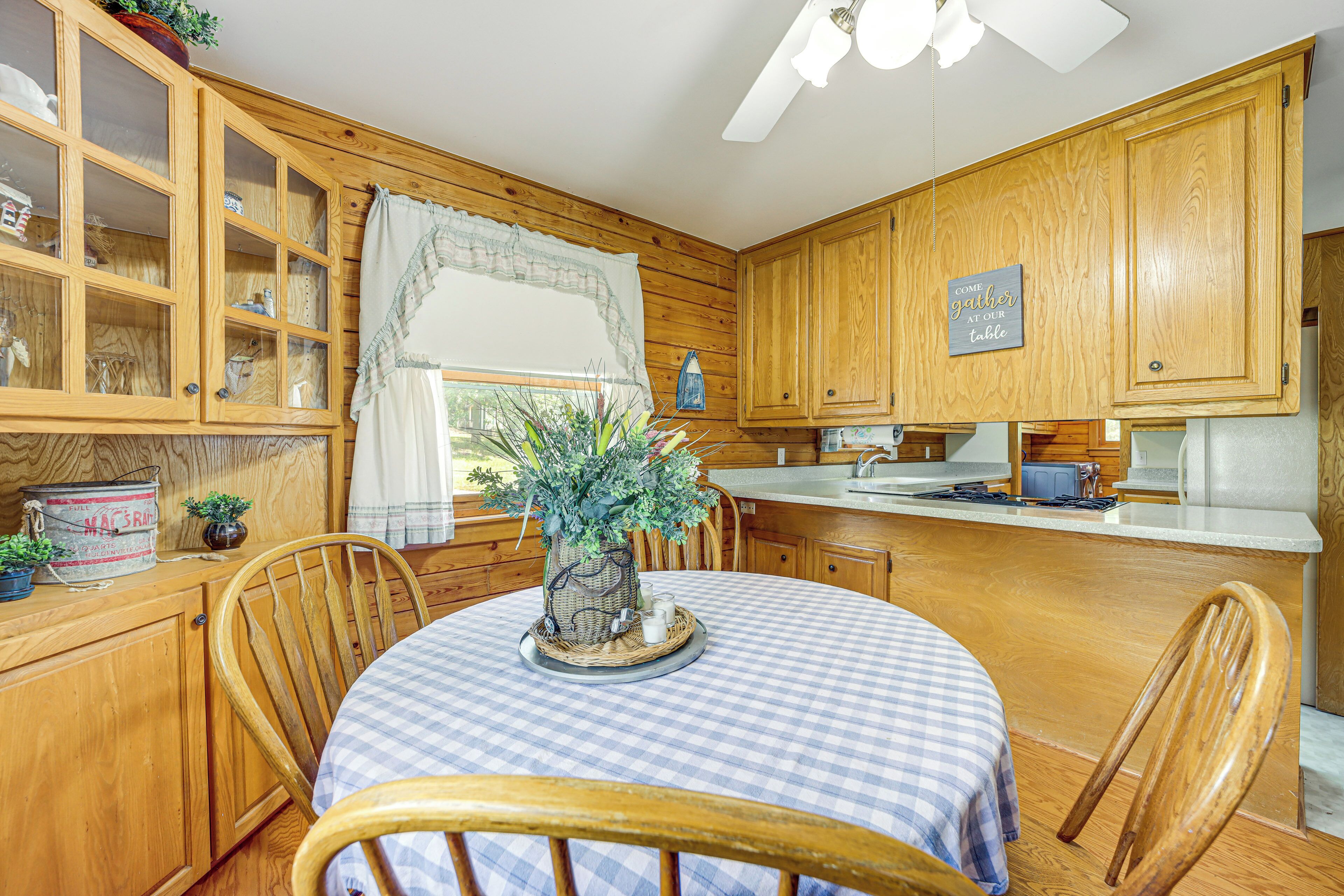 A wooden kitchen with a dining table set for two, featuring a checkered tablecloth and a centerpiece.