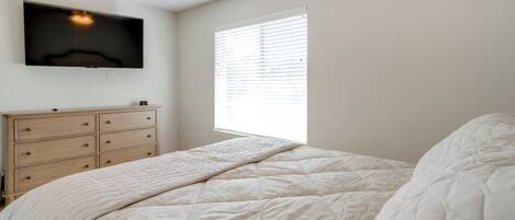 A bedroom with a bed, a dresser, a TV mounted on the wall, and a window with blinds.