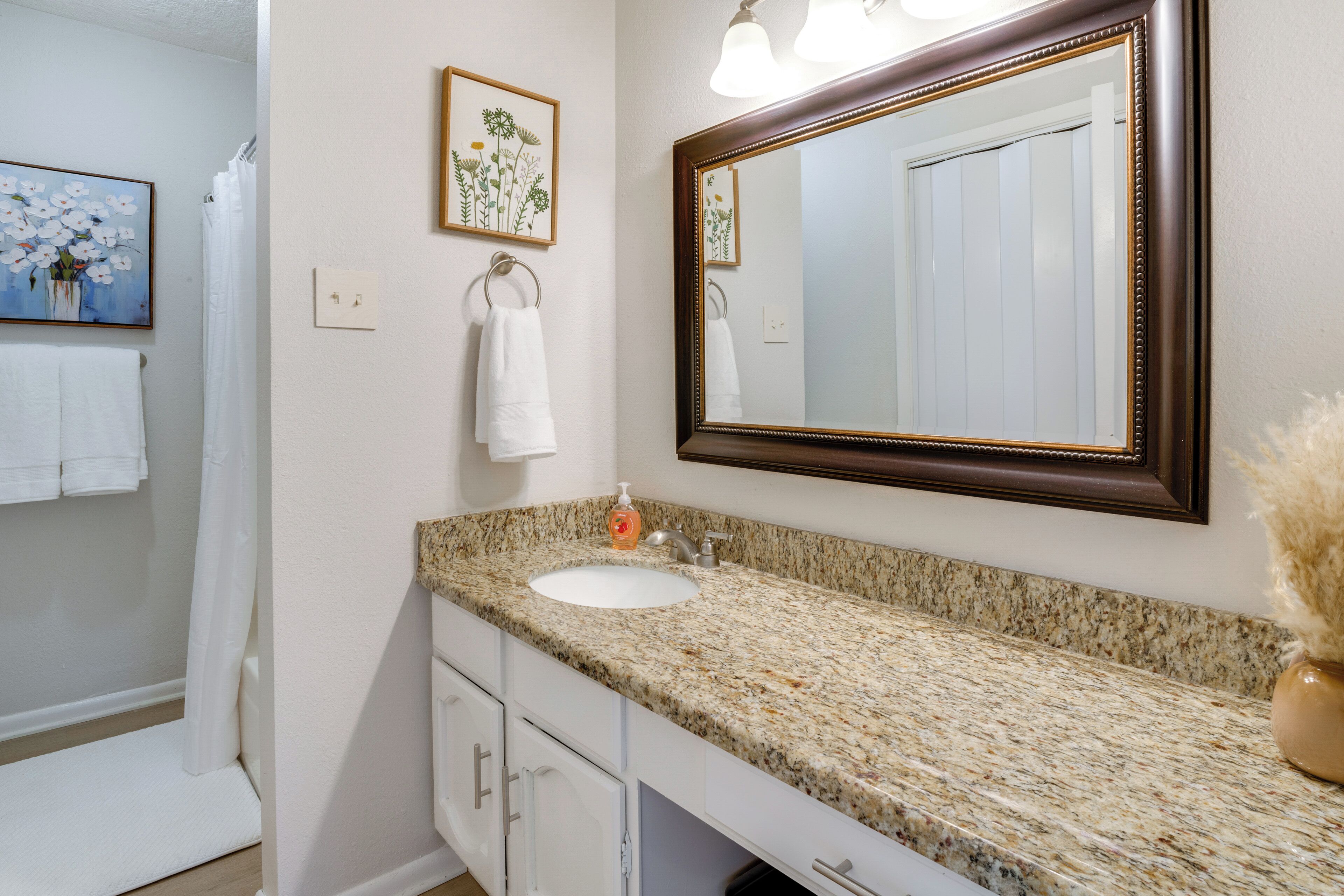 A bathroom with a granite countertop sink, a large mirror, and a shower curtain.