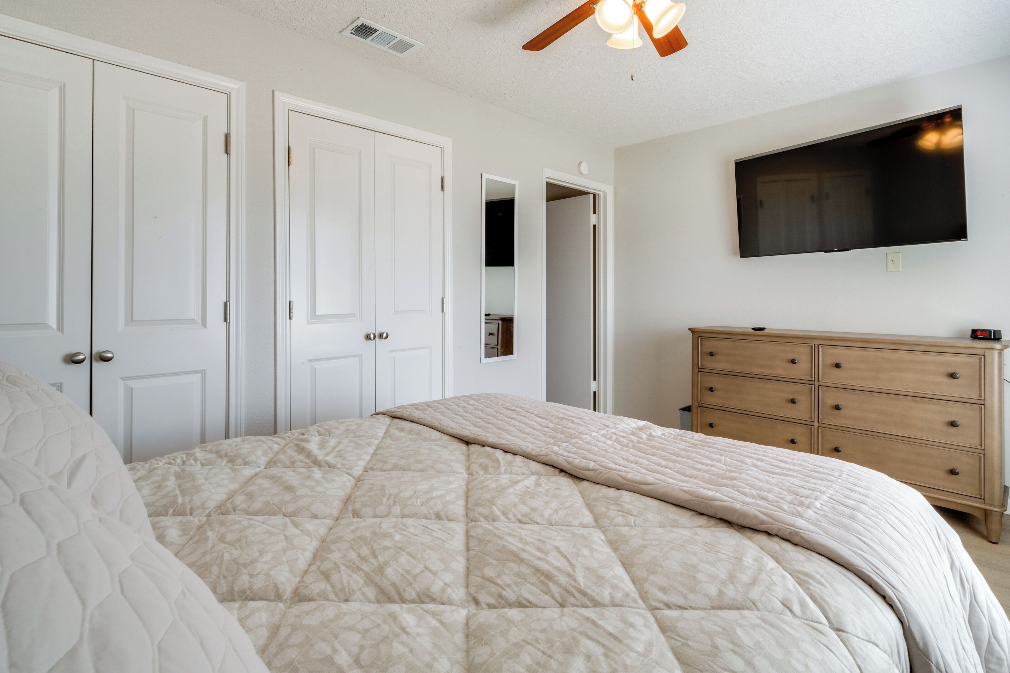 Un dormitorio con cama, cómoda, televisor y ventilador de techo.