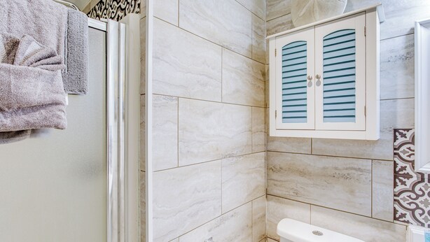 A bathroom with a toilet, a towel rack with towels, and a cabinet with striped doors. - 'shore Drive Serenity' - Steps to Ocean Annies! (Myrtle Beach)