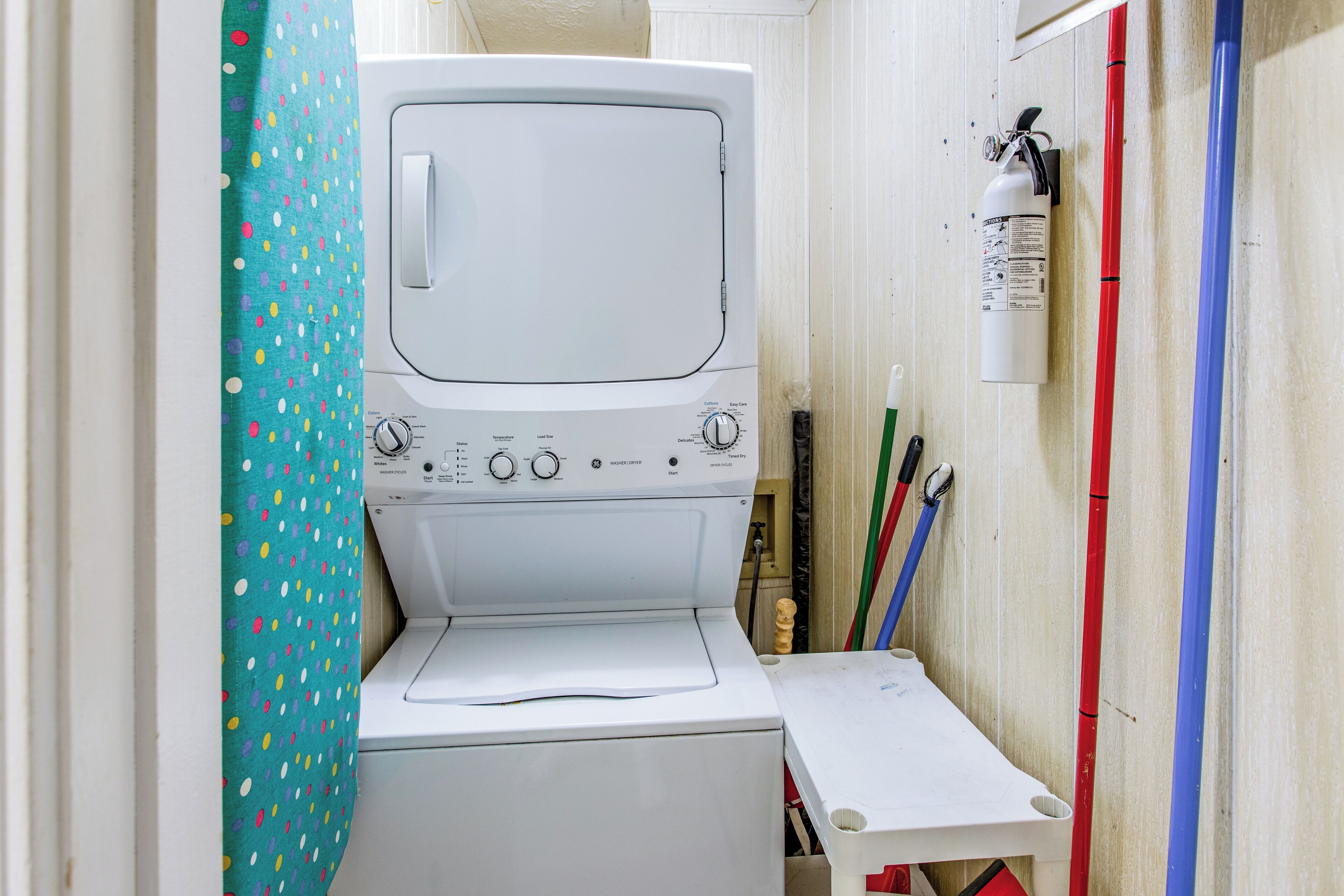 A compact laundry room with a washing machine, a drying machine, and a fire extinguisher mounted on the wall.