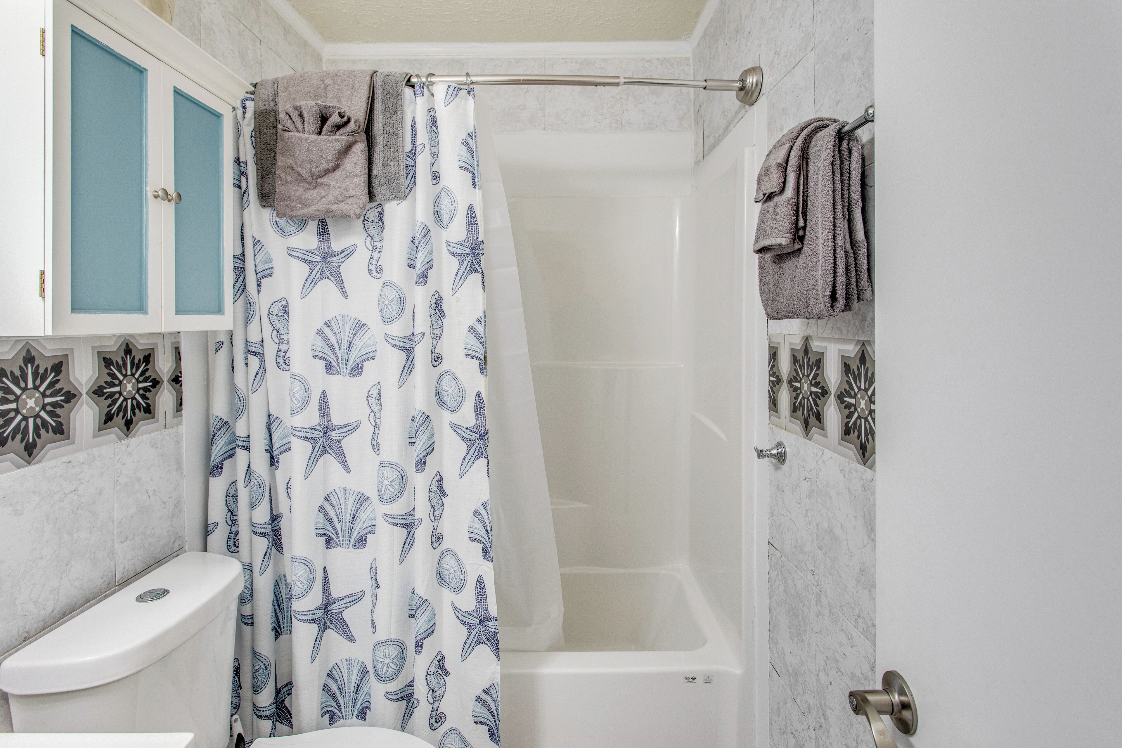 Une salle de bain avec un rideau de douche orné d’un motif représentant des étoiles de mer et des coquillages, des toilettes et une baignoire.