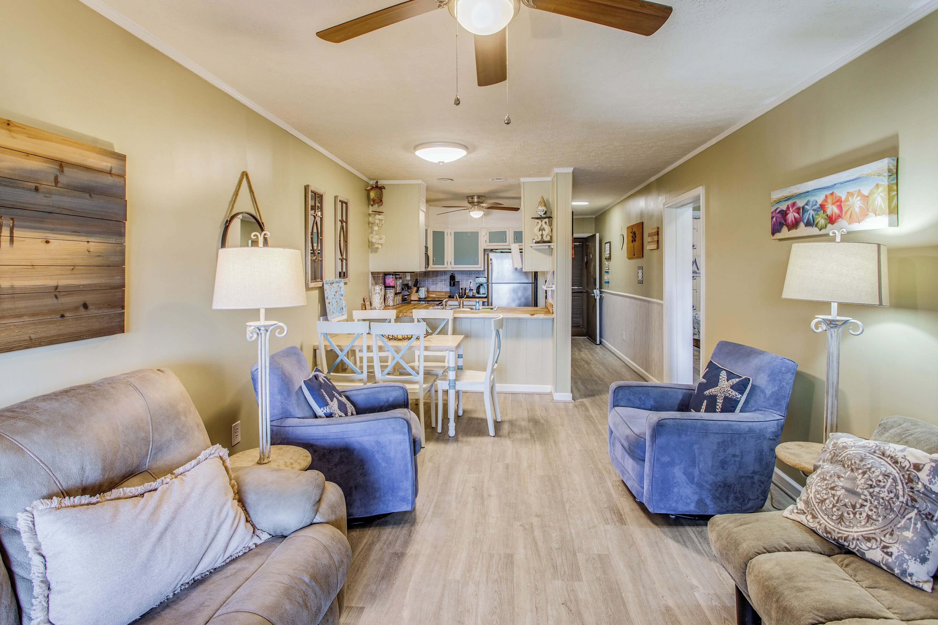 A spacious living room with a dining area, a kitchen in the background, and a ceiling fan.