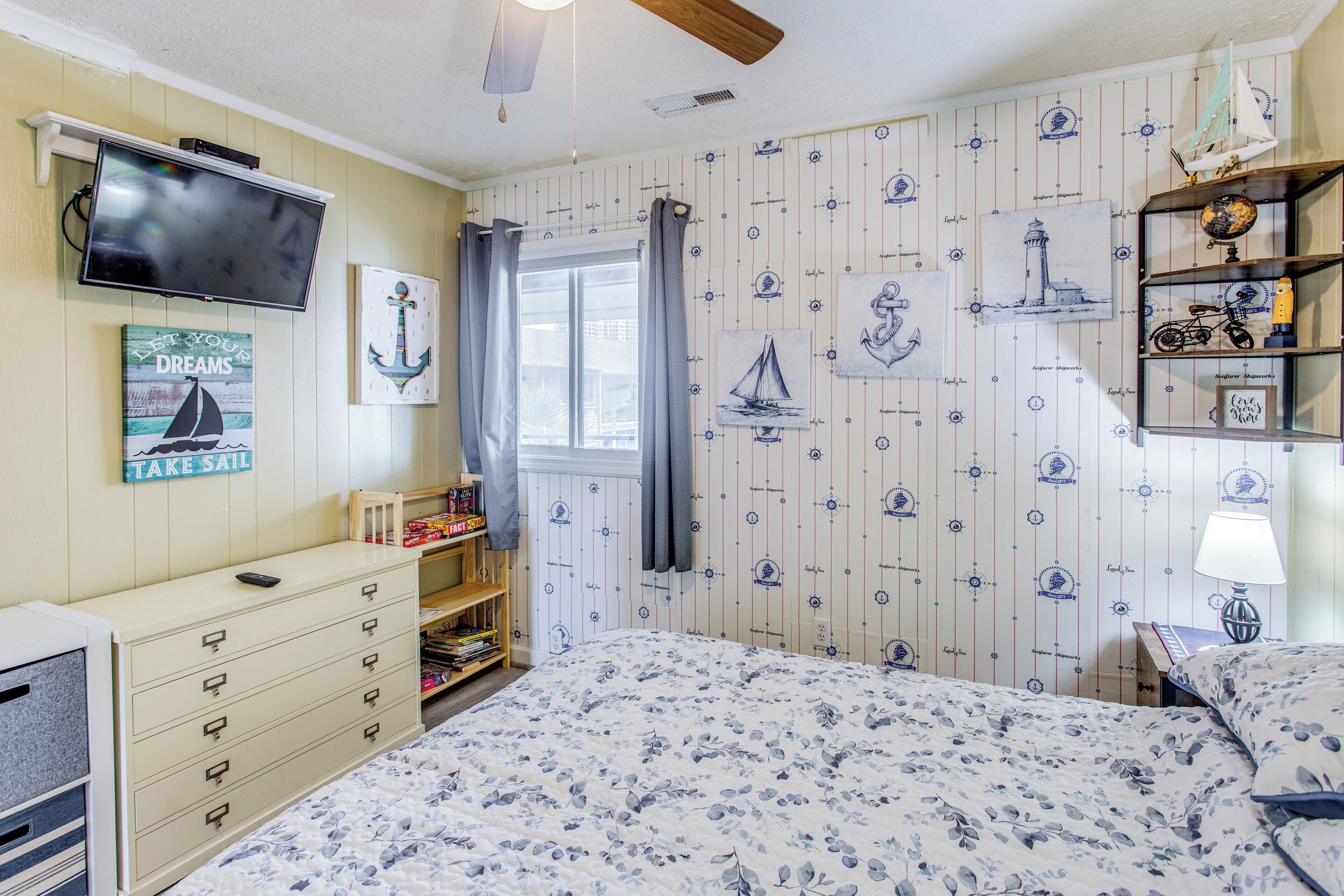 Een slaapkamer met een bed, een dressoir, een televisie en behang met een nautisch thema.