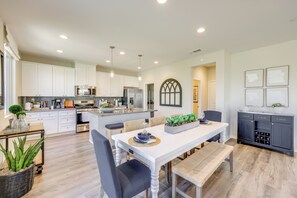 Una cocina moderna con armarios blancos, electrodomésticos de acero inoxidable y una zona de comedor con mesa y banco blancos.