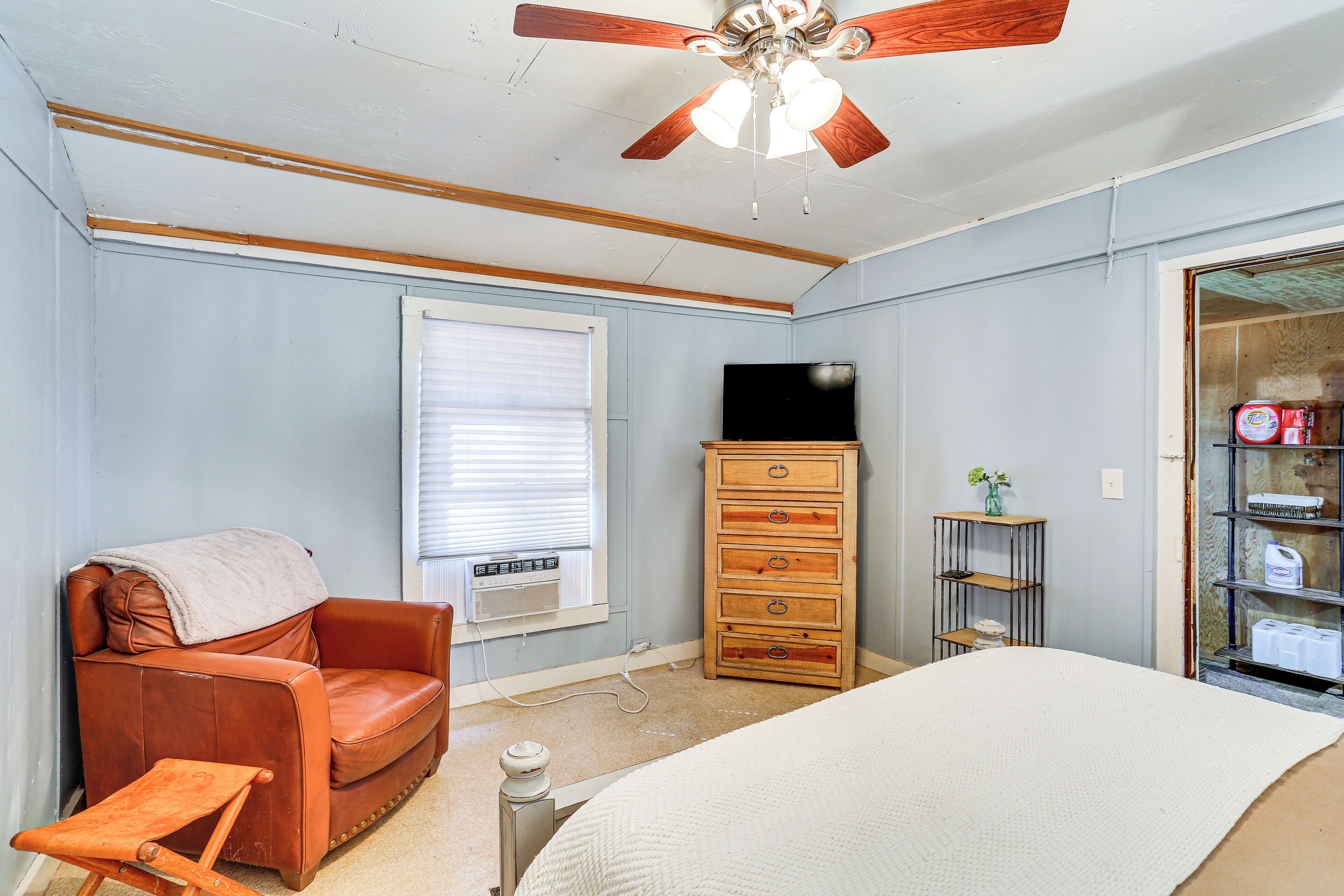 A bedroom with a bed, a wooden dresser, a leather chair, a ceiling fan, and a window with blinds.