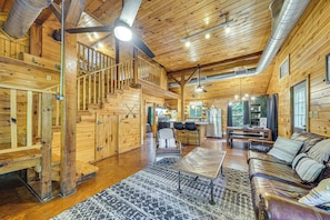 Un intérieur de chalet en bois spacieux, comprenant un escalier, un coin repas et un salon avec un canapé en cuir.
