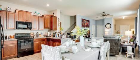 A spacious kitchen with wooden cabinets, a black microwave, and a stove. There is a dining area with a table set for four, surrounded by chairs.