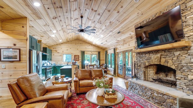 A cozy cabin interior with a stone fireplace, leather furniture, and a large TV mounted on the wall. - Hot Tub, Trail Access & 400 Acres on Lavender Mtn! (Rome)