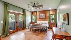 A bedroom with a wooden floor, a bed with white bedding, a wooden bench, a desk, a chair, a ceiling fan, and a window with curtains. - Hot Tub, Trail Access & 400 Acres on Lavender Mtn! (Rome)