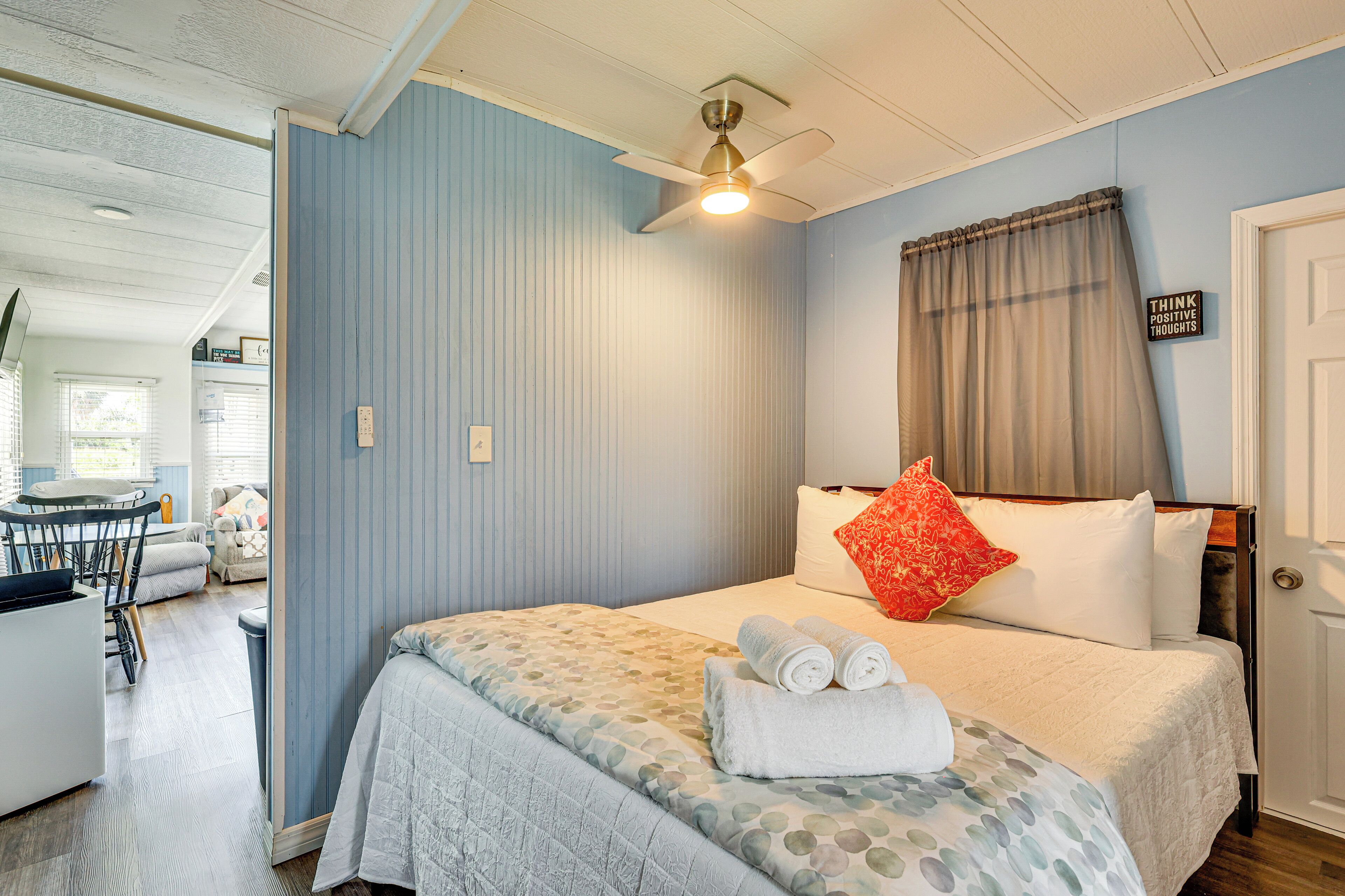 A bedroom with a bed, a ceiling fan, a window with curtains, and a sign on the wall.