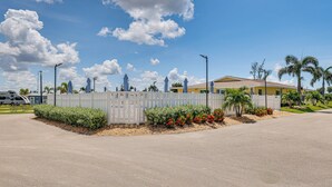 A gated parking area with a white fence, palm trees, and red flowers. - 3 Mi to Ft Myers Beach: Coastal Home Near Leetran! (Fort Myers Beach)