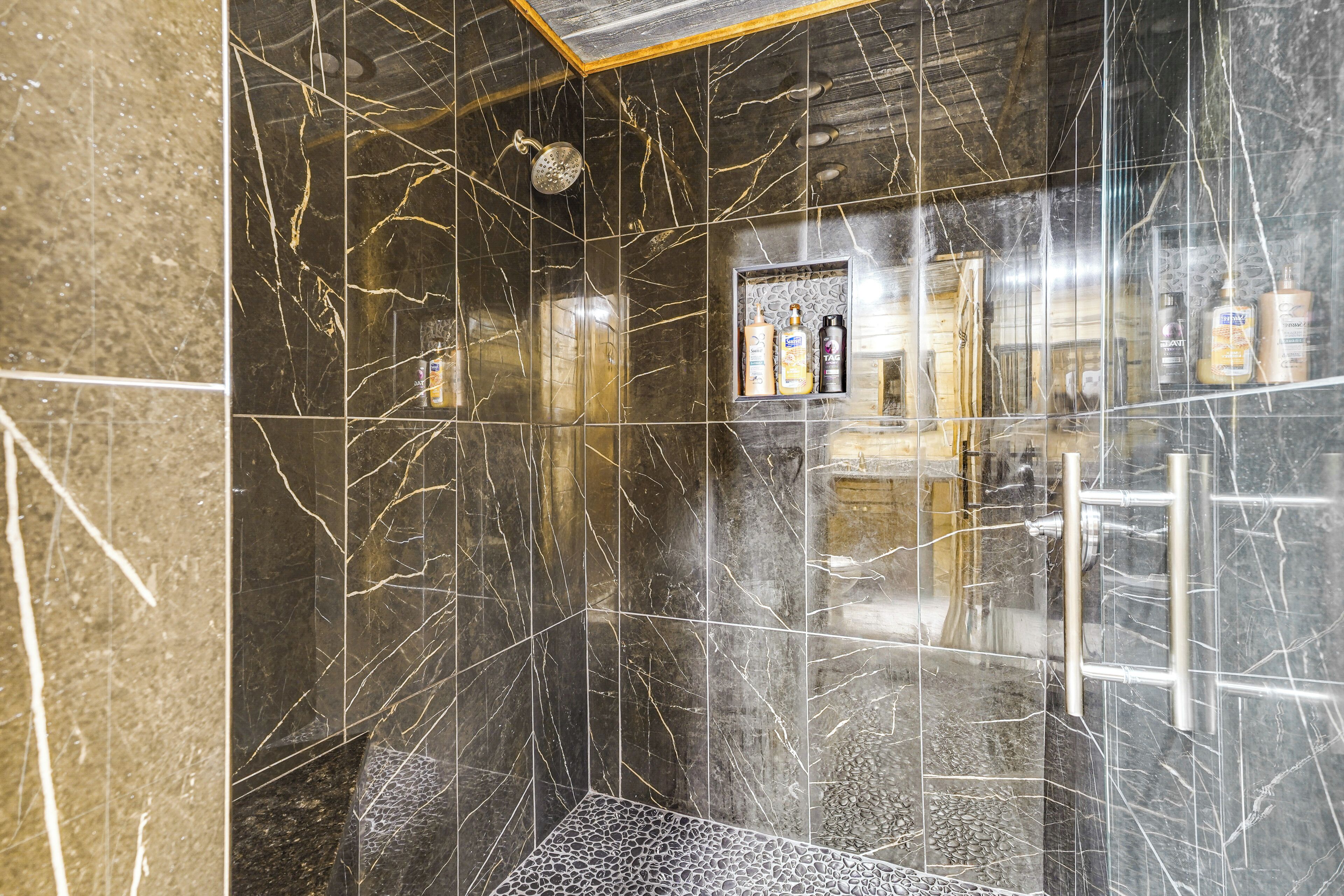 Un baño con cabina de ducha de vidrio, paredes de mármol y un estante con artículos de aseo.