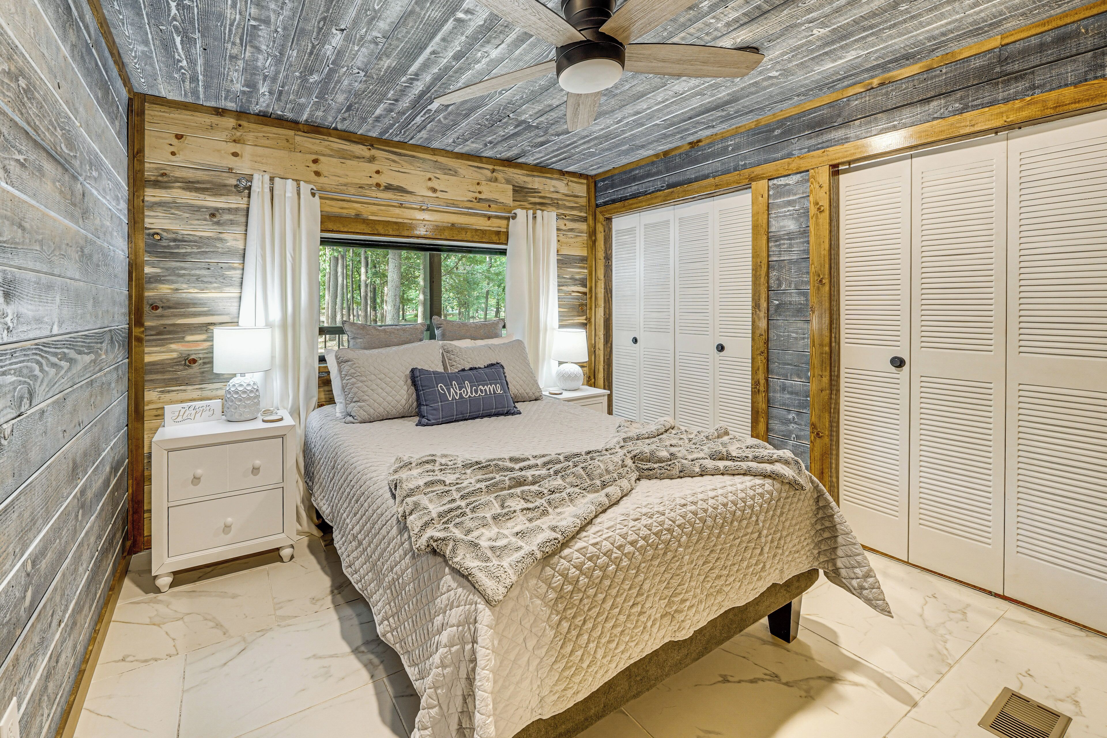 A bedroom with a wooden ceiling, a bed with a quilt, a nightstand with a lamp, and a window with curtains.