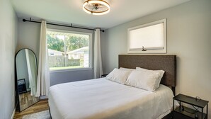 A neatly arranged bedroom with a large bed, a bedside table, a ceiling fan, and a window with curtains.