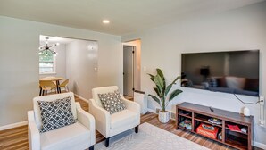 A living room with two white armchairs, a coffee table, a flat-screen TV, a wooden entertainment unit, and a potted plant.