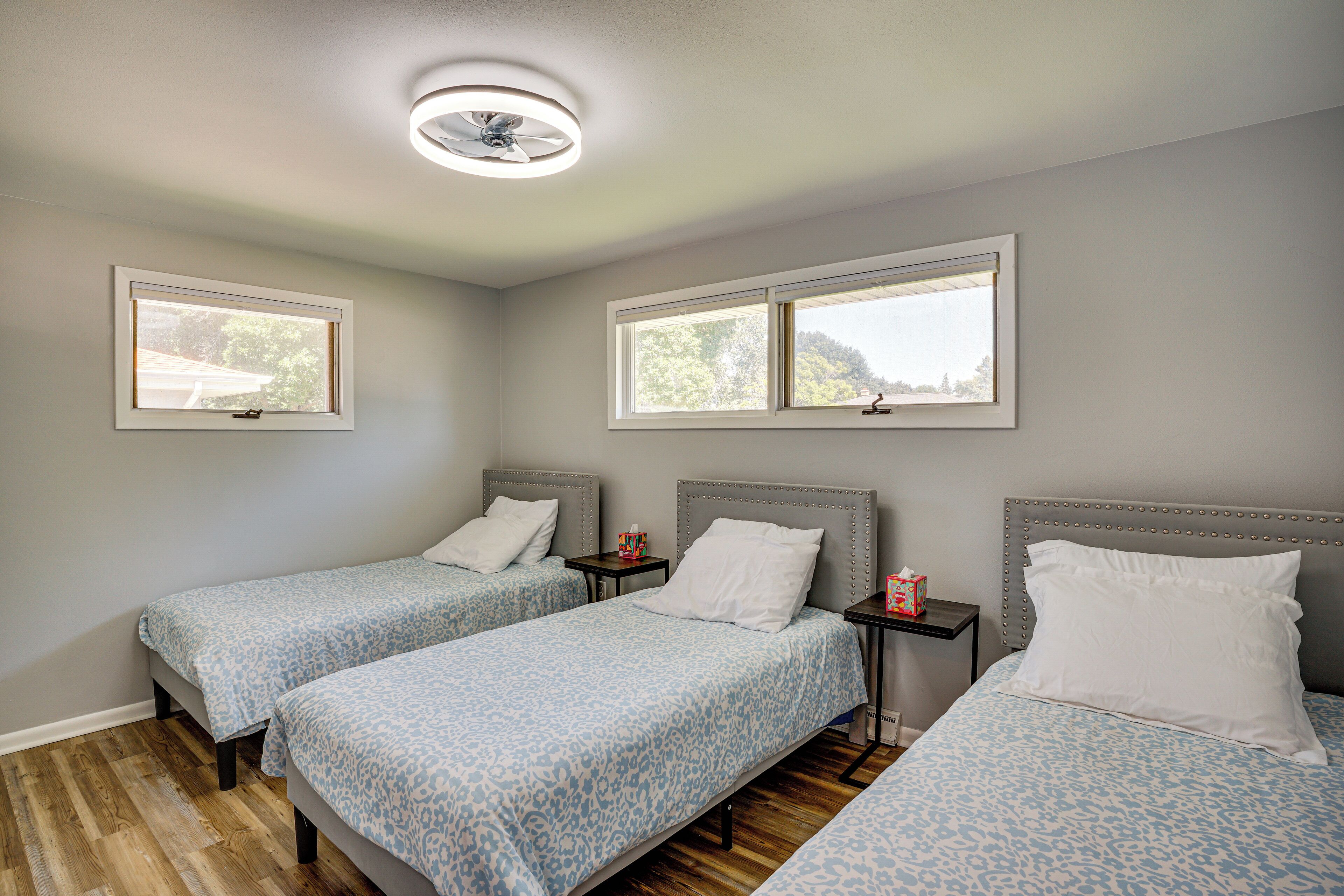 A room with two beds, each with a headboard and footboard, a small table with a box of tissues, and a ceiling fan.