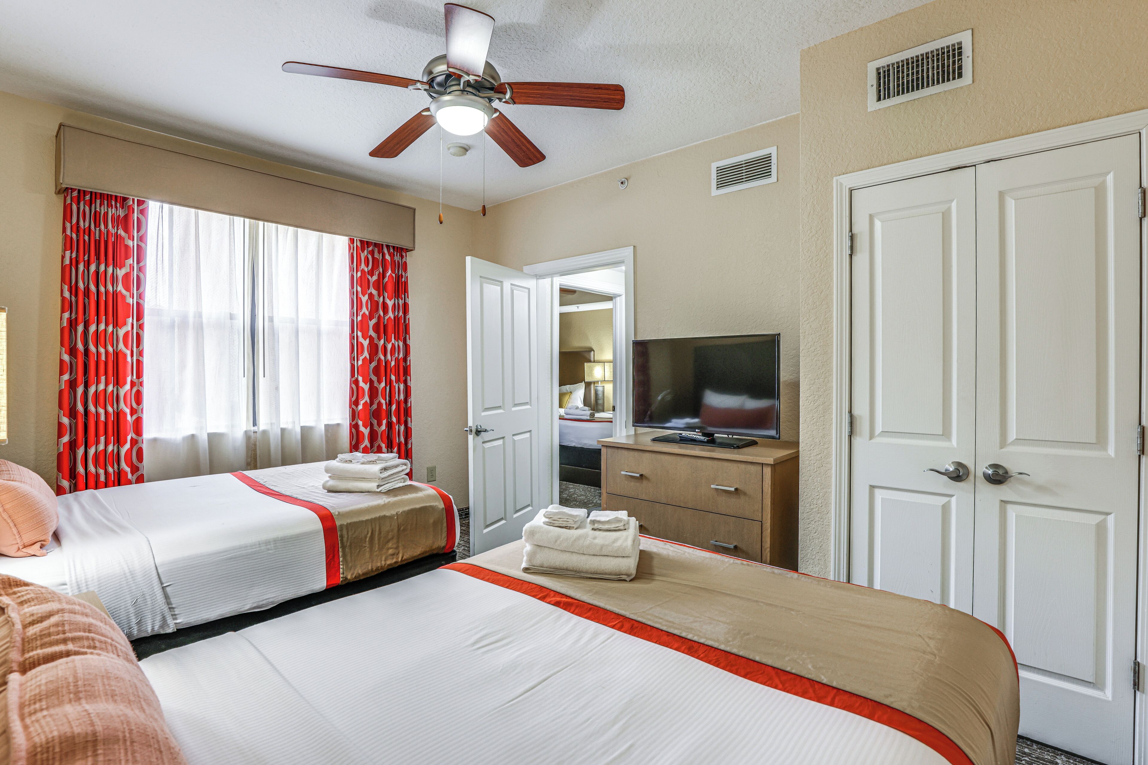 Une chambre d’hôtel avec deux lits, un ventilateur de plafond, une télévision et une armoire.