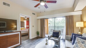 A hotel room with a TV, a sofa, a coffee table, a ceiling fan, and a balcony with curtains. - Poolside Oasis: 7 Mi to Disney & Universal (Orlando)