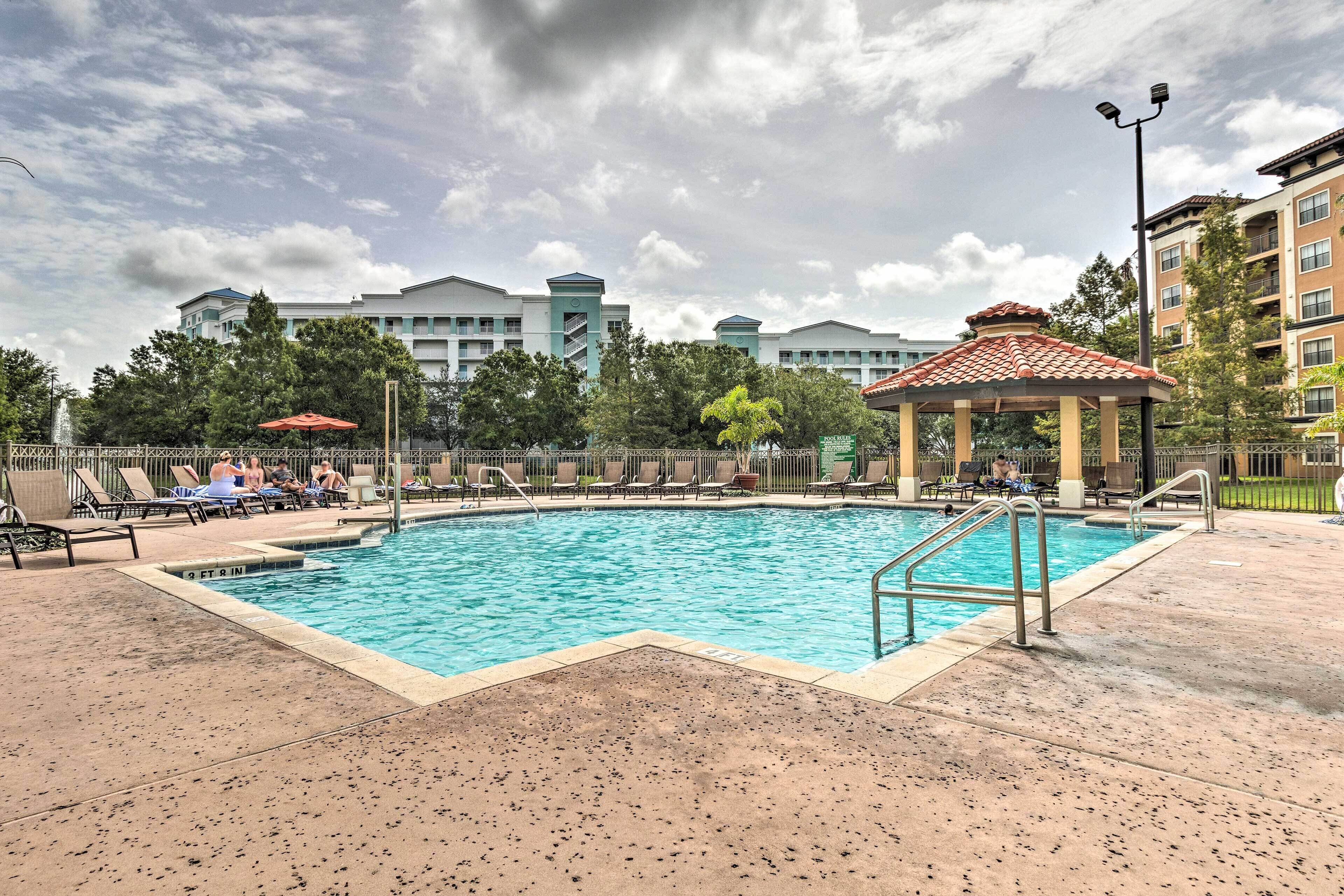 A swimming pool with lounge chairs and a gazebo, surrounded by buildings and trees.
