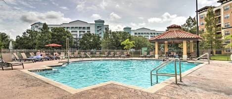 A swimming pool with lounge chairs and a gazebo, surrounded by buildings and trees.
