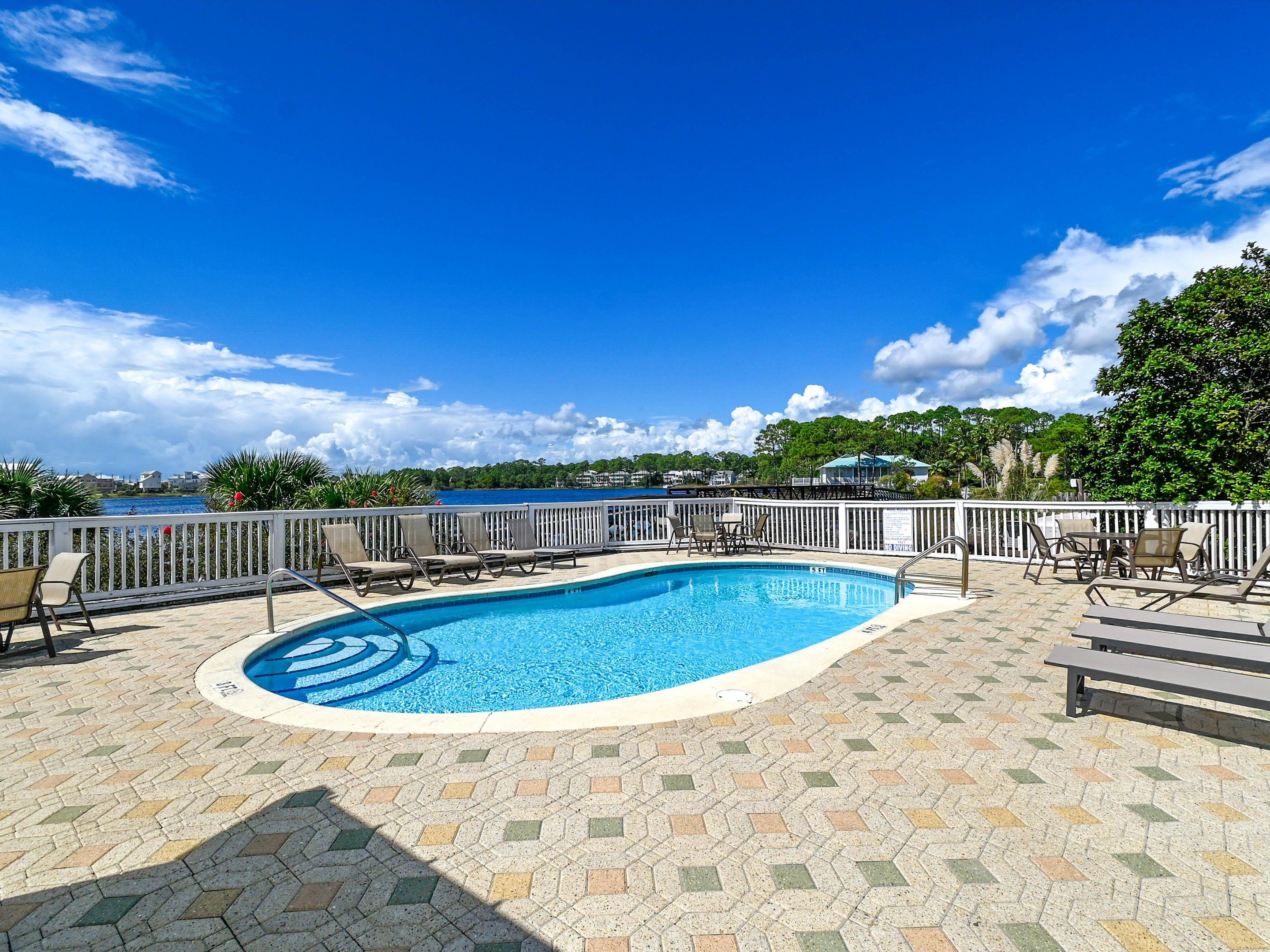 A swimming pool with a view of the sea, surrounded by lounge chairs and a tiled deck.
