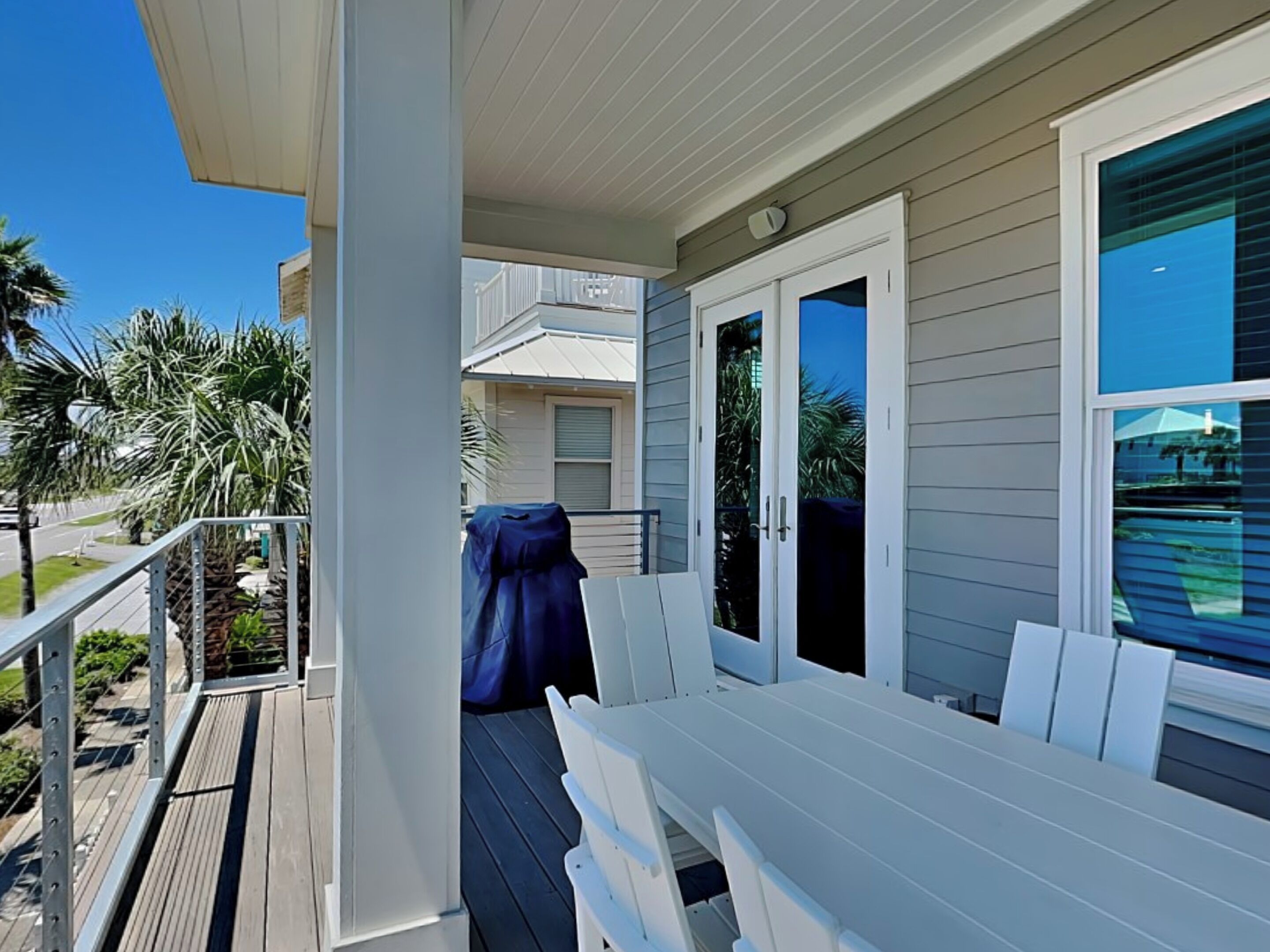 A covered porch with white railings, a barbecue grill, and a seating area with white chairs.